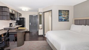 A hotel room with a bed, desk, chair, and kitchenette.