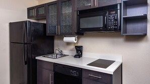 A compact kitchen with dark cabinetry, a stainless steel refrigerator, a microwave, a coffee maker, and a dishwasher.