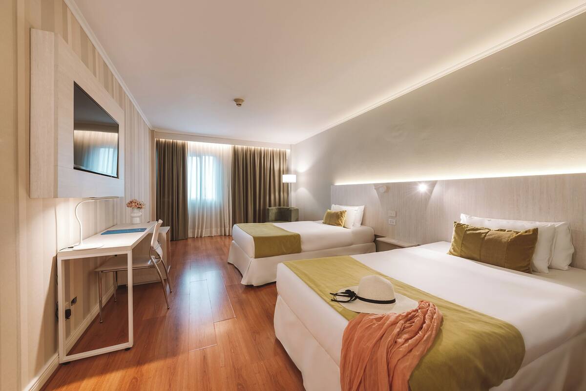 Une chambre d’hôtel avec deux lits, un bureau, une télévision et une fenêtre avec des rideaux.