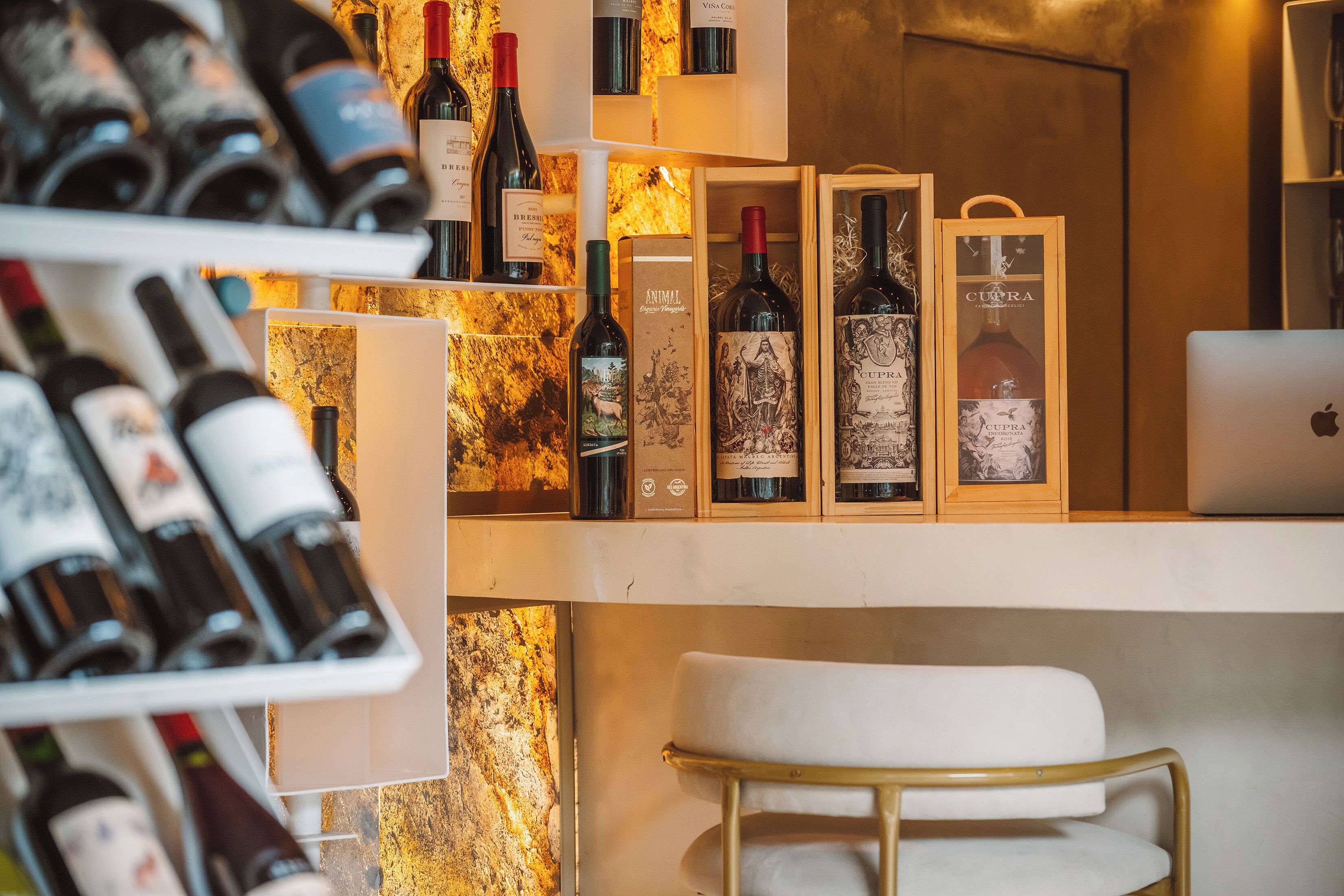 A wine display with bottles and boxes, a laptop, and a white chair.