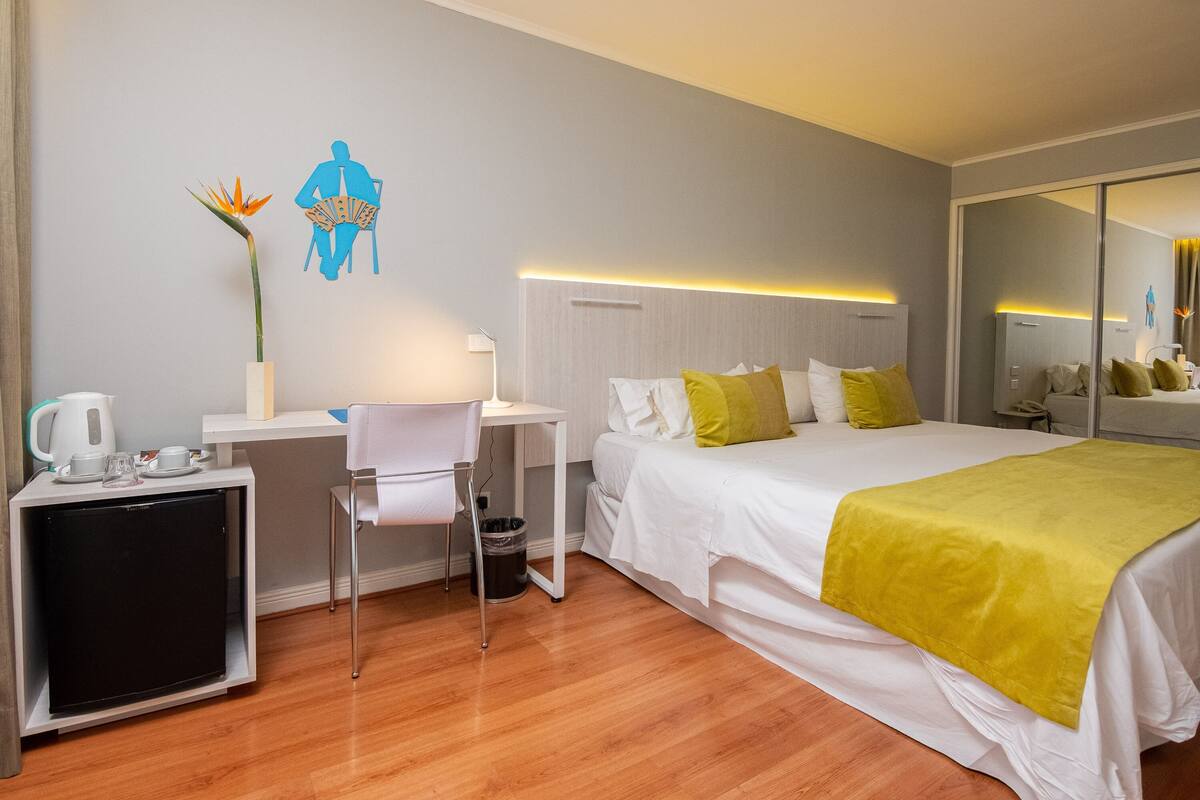 Une chambre d’hôtel équipée d’un lit, d’une table de chevet, d’une chaise, d’un bureau et d’un petit réfrigérateur.