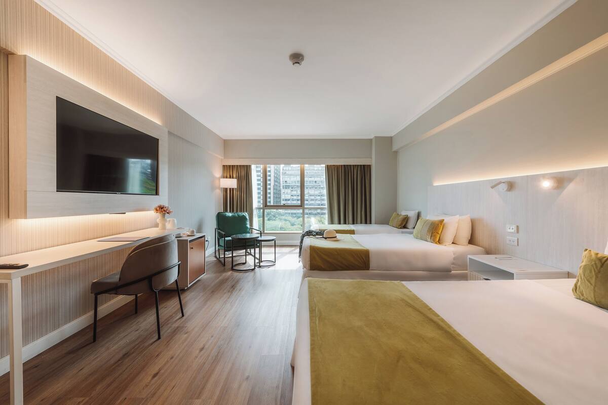 Une chambre d’hôtel moderne équipée d’une télévision à écran plat, d’un bureau, d’une chaise, de deux lits, d’une fenêtre avec des rideaux et offrant une vue sur la ville.