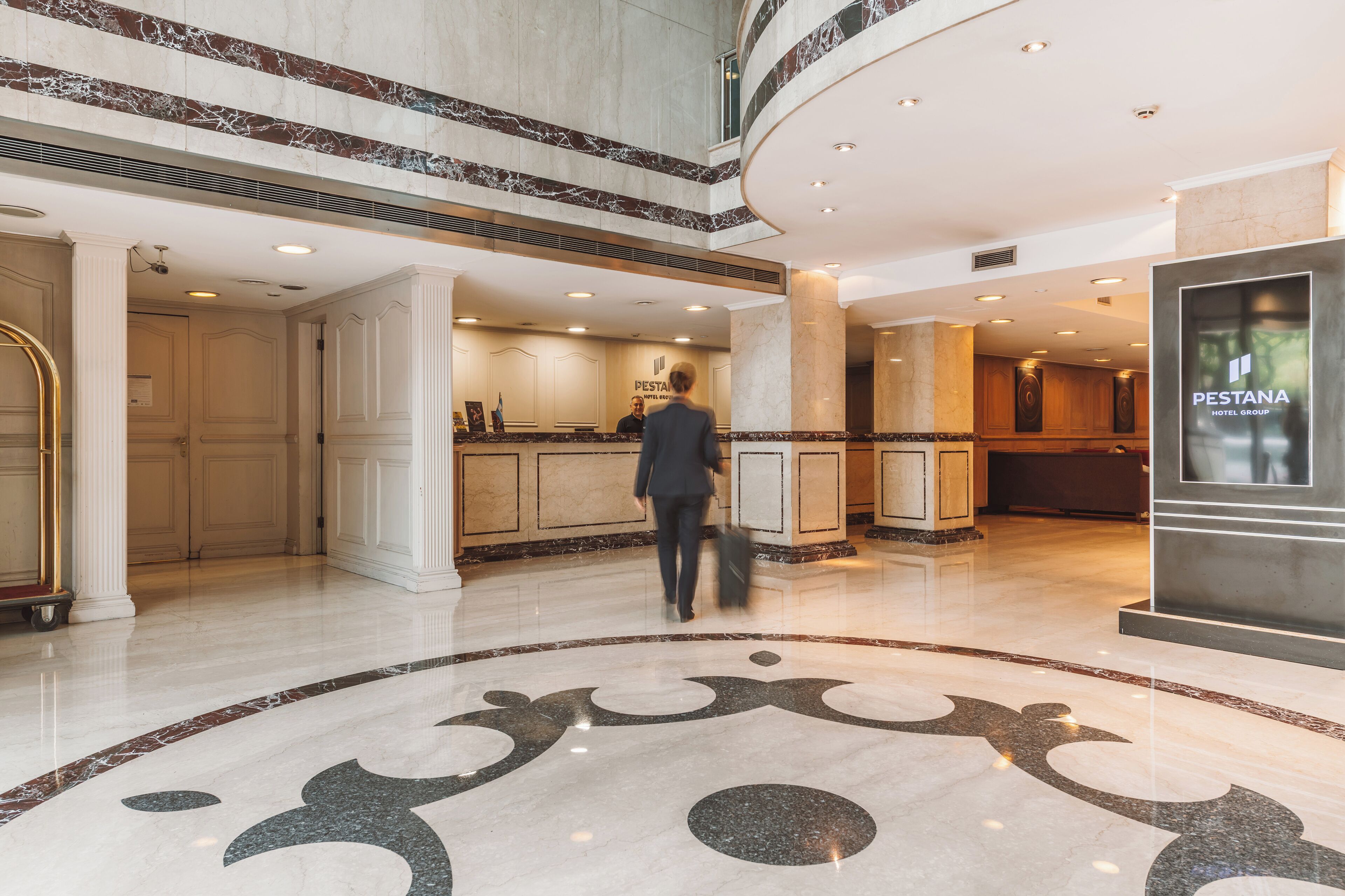 Um saguão de hotel com piso de mármore, um balcão de recepção e uma placa do Grupo Pestana.
