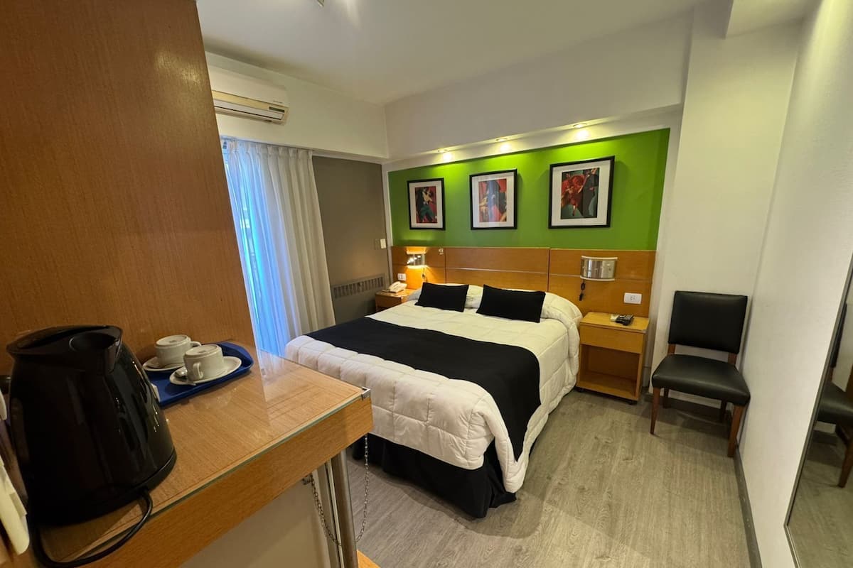 A hotel room with a bed, bedside table, chair, and a coffee maker.