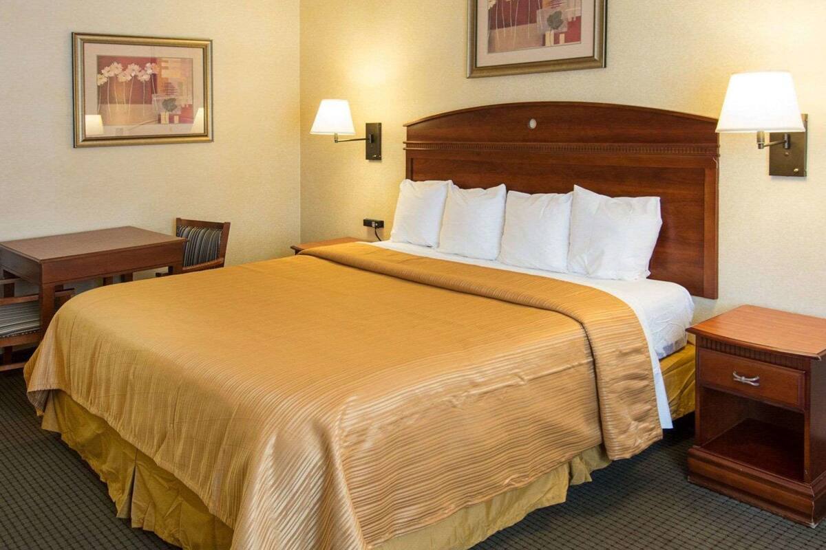 A hotel room with a large bed, two bedside tables, a desk, and two wall-mounted lamps.