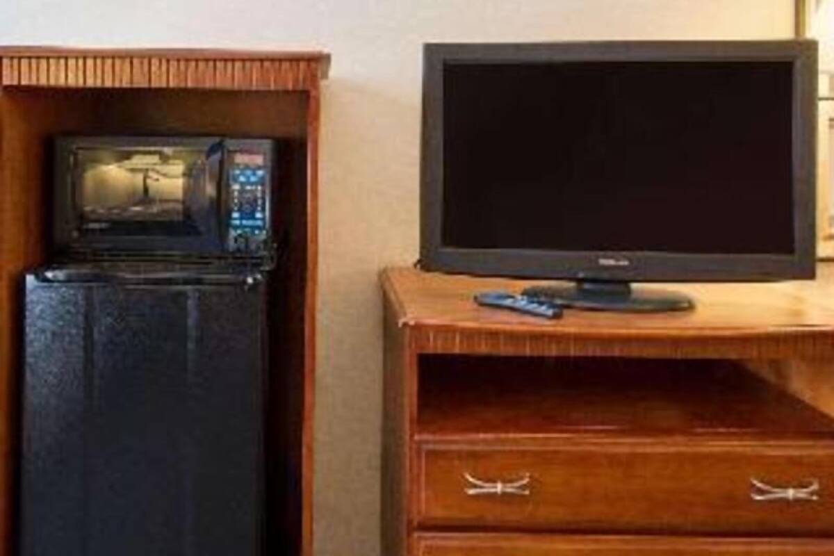 A room with a microwave, a television on a wooden stand, and a small drawer.