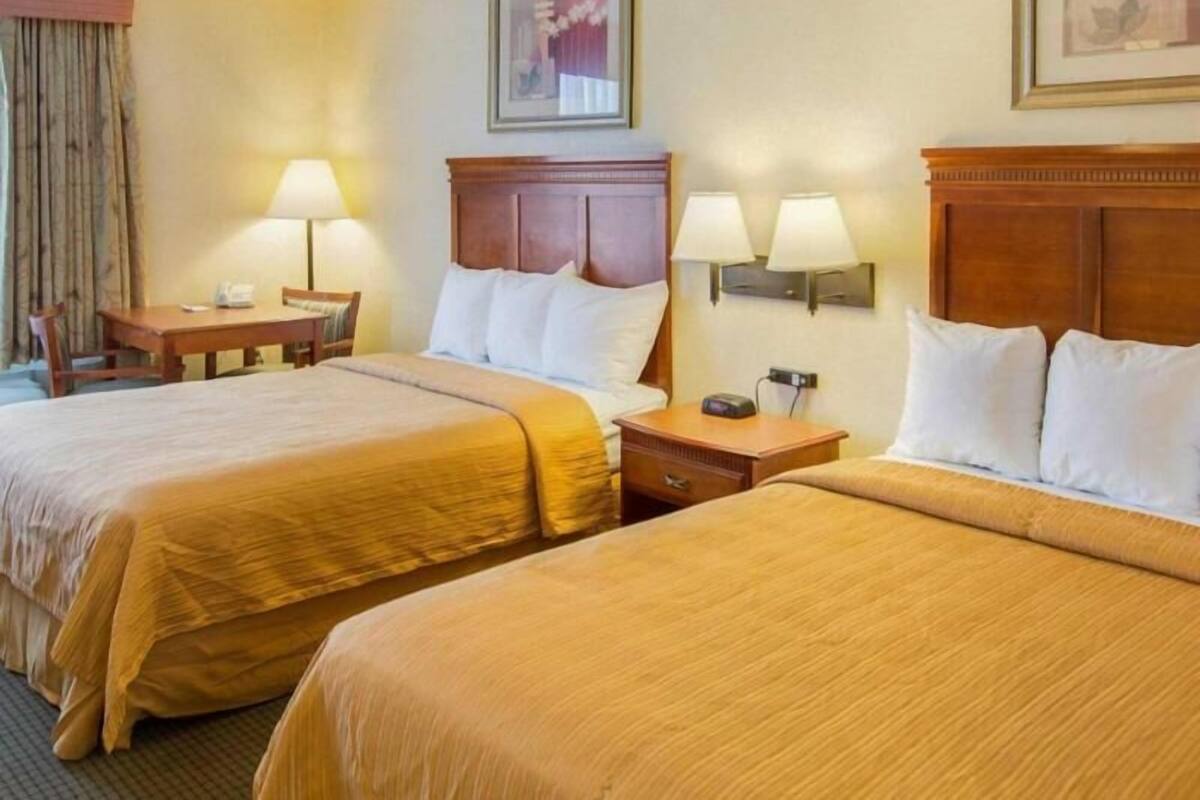 A hotel room with two beds, a desk, and two wall-mounted lamps.