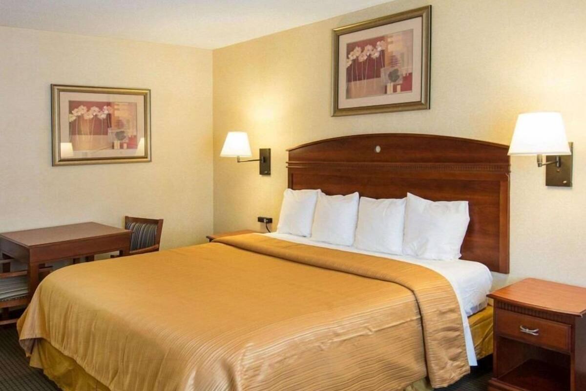 A hotel room with a large bed, bedside tables, a desk, and two wall-mounted lamps.