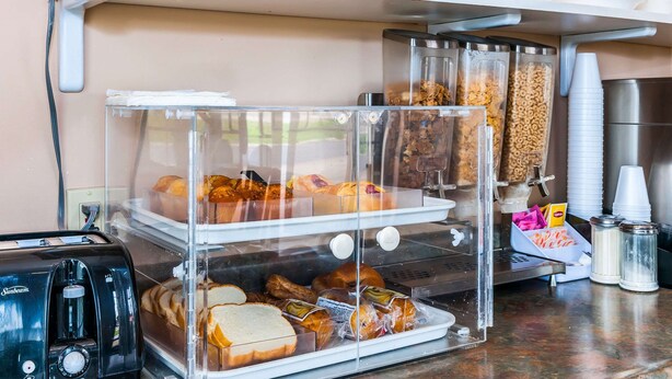 Una vitrina de pastelería con diversos productos horneados, una máquina de café y recipientes para condimentos.
