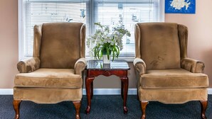 Dos sillones marrones con una mesa de vidrio y un jarrón con flores blancas en el centro.