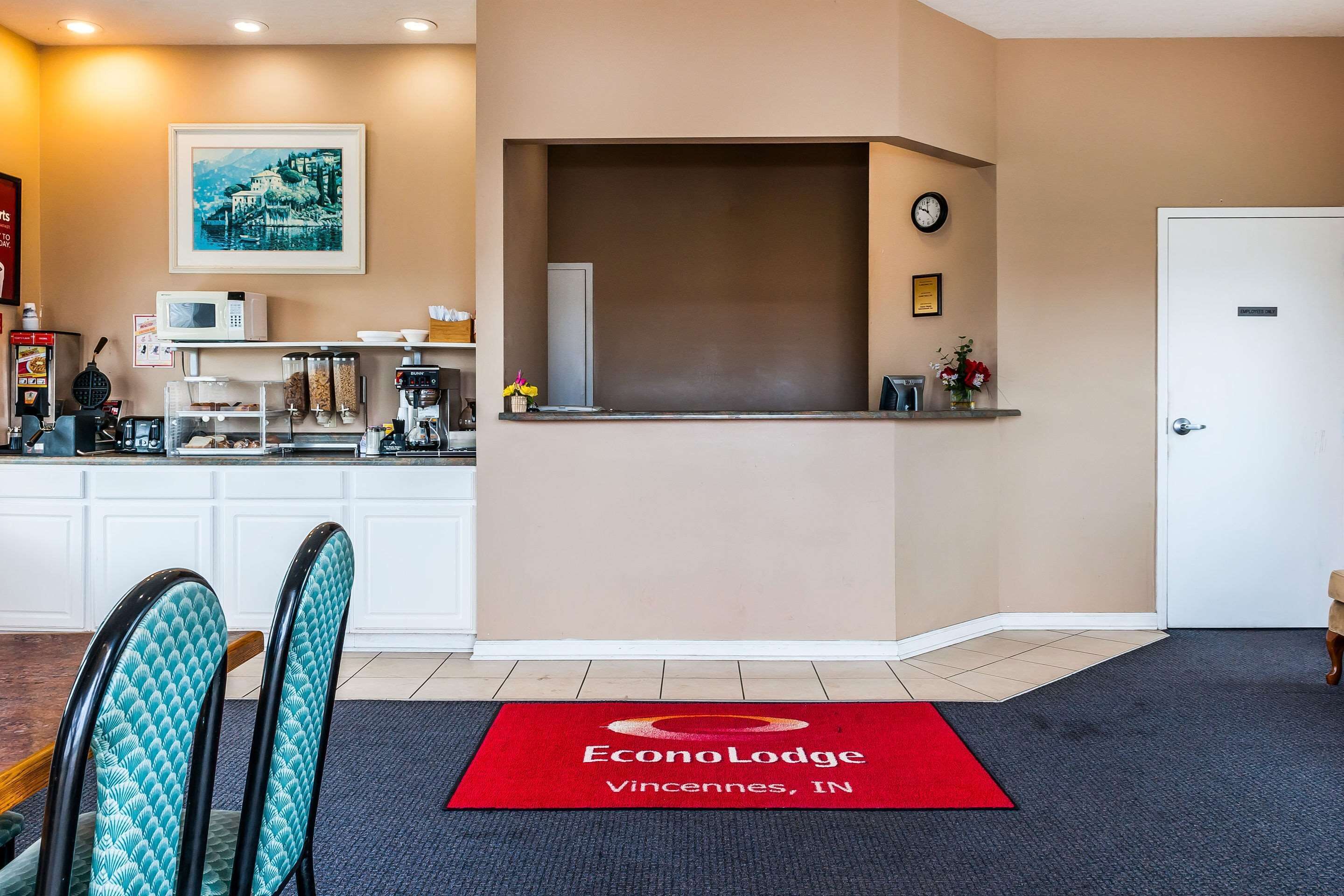 A reception area with a red doormat, a clock, and a framed picture on the wall.