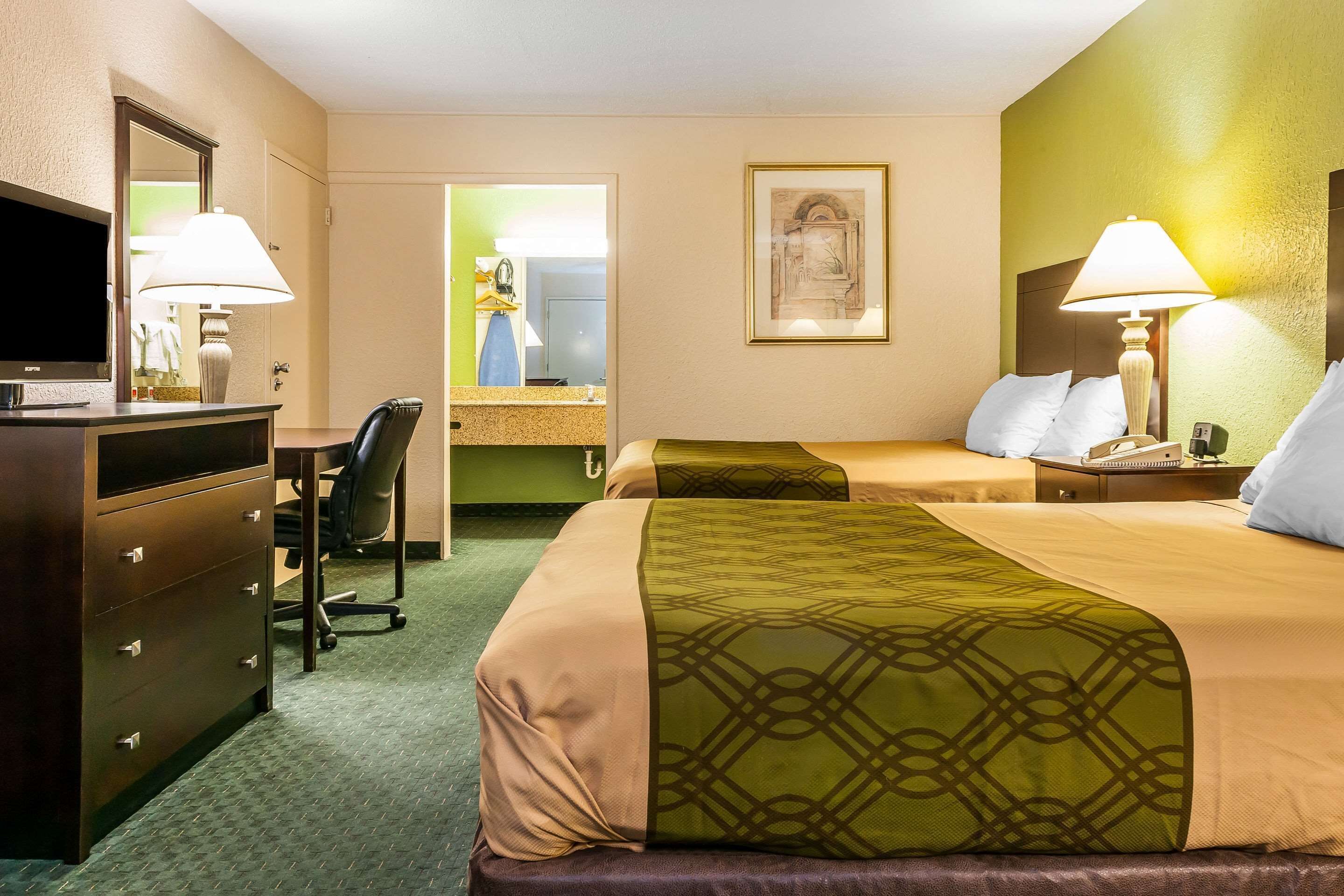 Ein Hotelzimmer mit zwei Betten, einem Schreibtisch mit Stuhl, einem Schminktisch und einem Fernseher.