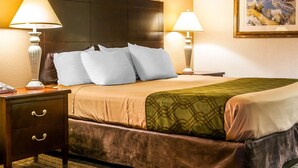 Una habitación de hotel con una cama grande, dos mesitas de noche con lámparas, una mesita con cajones y un cuadro en la pared.