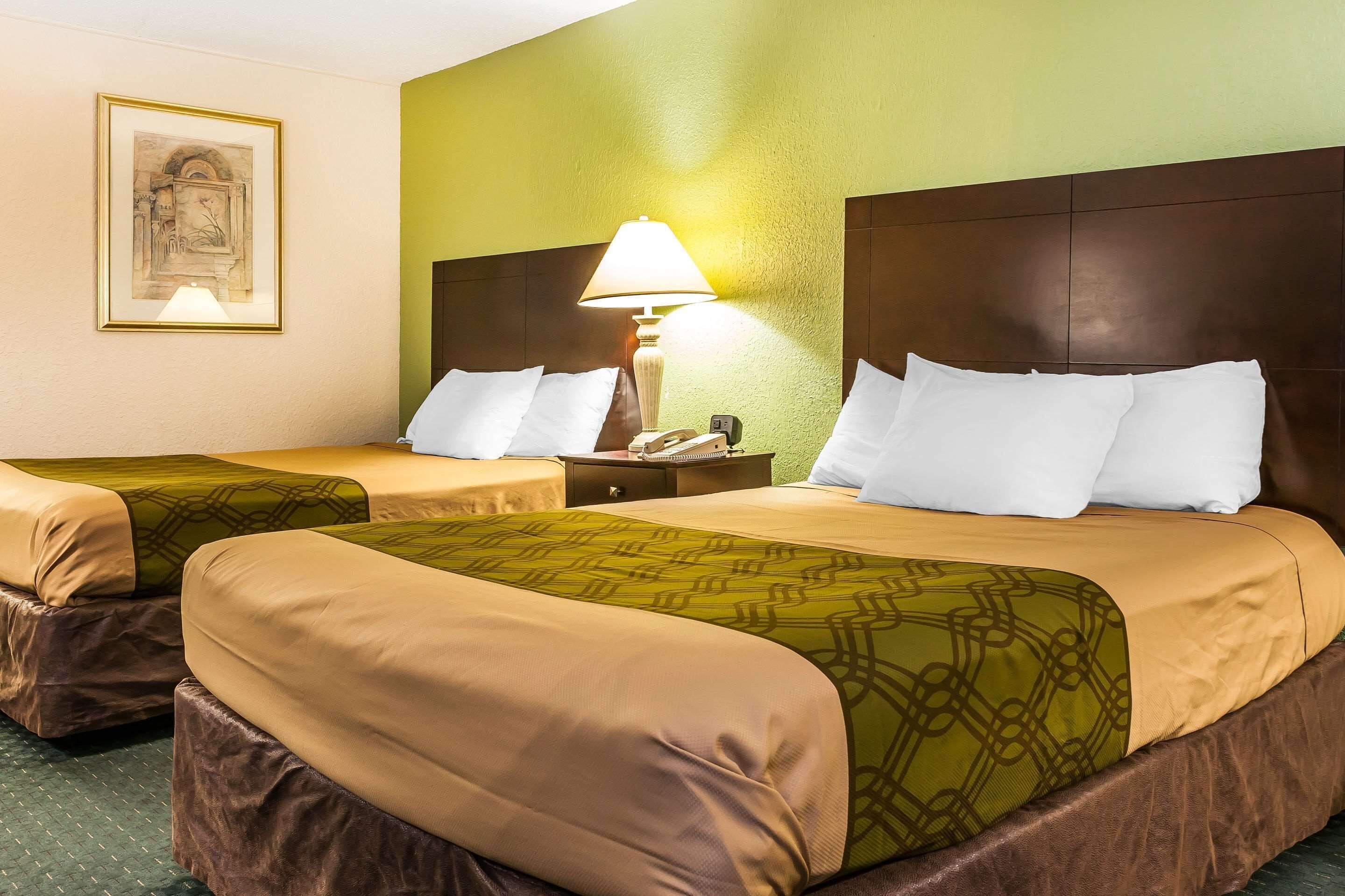 A hotel room with two beds, each with a headboard, a bedside table with a lamp, and a framed picture on the wall.