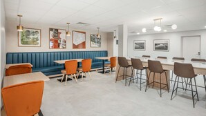 A modern dining area with a blue booth, orange chairs, and a long table. - Best Western River Cities (Russell)