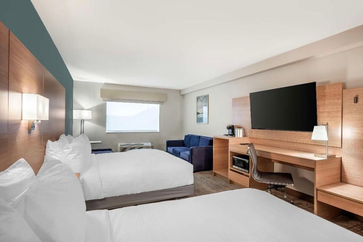 A hotel room with two beds, a desk, a chair, a television, and a window.