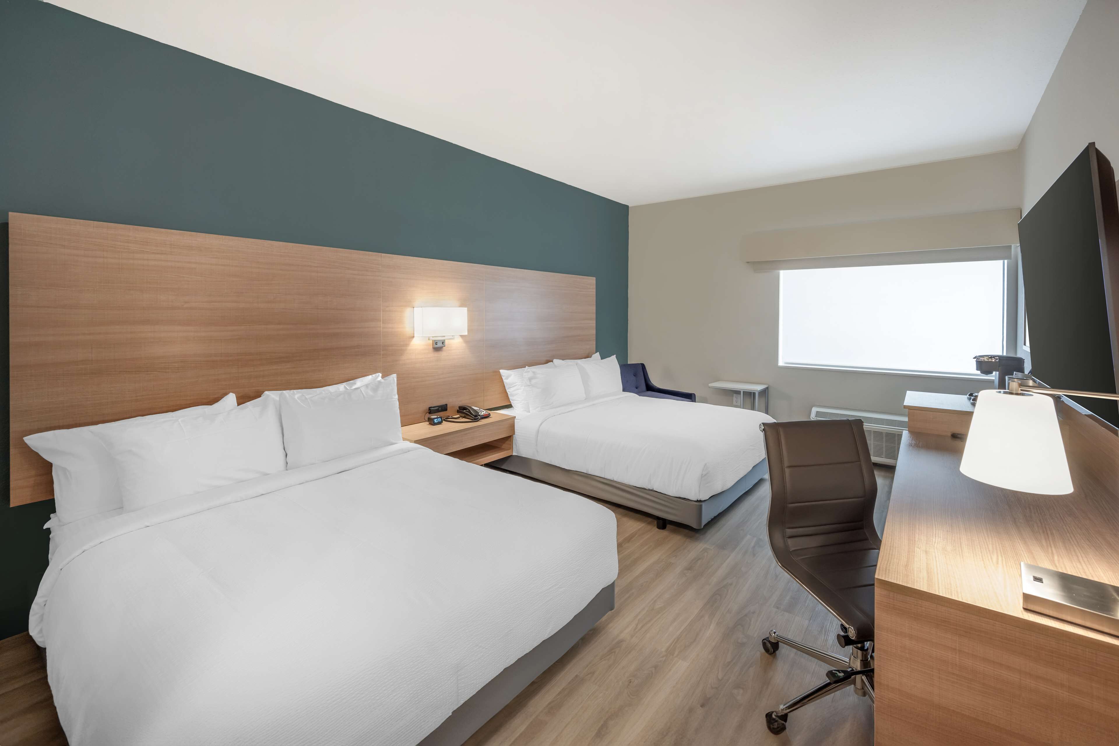 Habitación de hotel con dos camas, un escritorio, una silla, un televisor y una ventana.