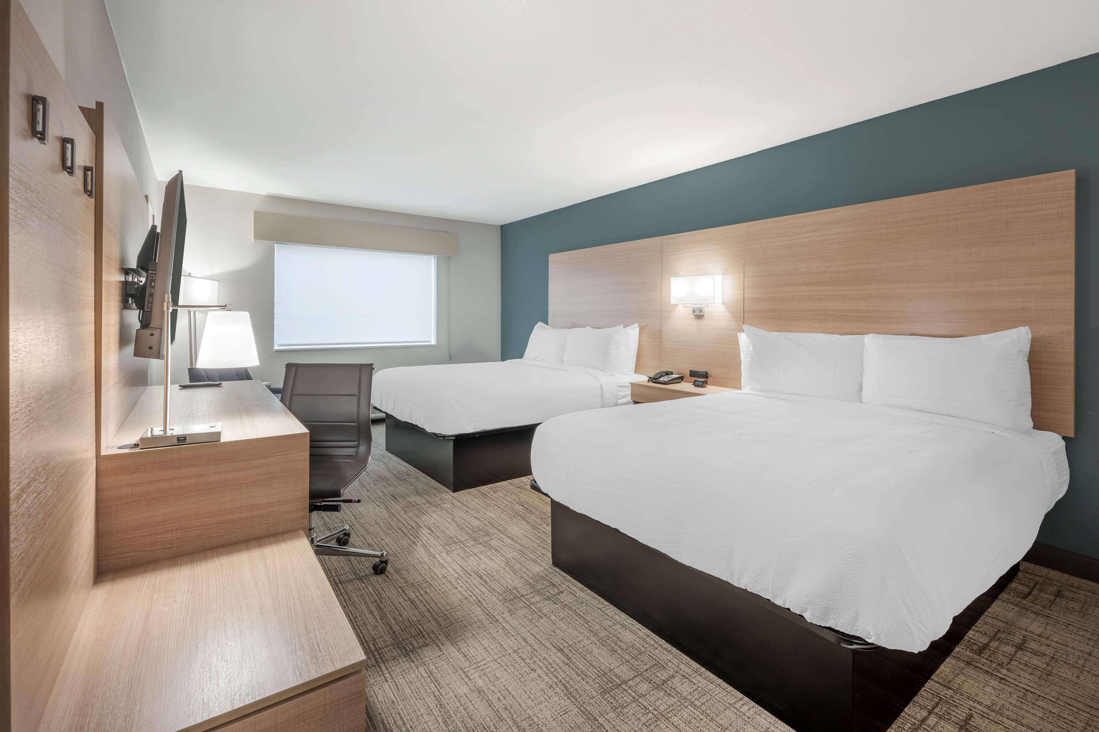 A hotel room with two beds, a desk, a chair, a TV, and a window.