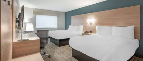 A hotel room with two beds, a desk, a chair, a TV, and a window.