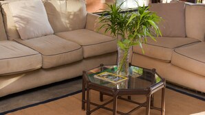 A beige sofa with a glass coffee table in front, a vase with a plant, and a magazine on the table. - Coco Beach Hotel (Sardinal)