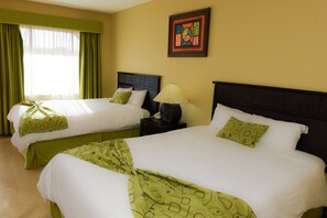 Two twin beds with green and white bedding, a bedside table with a lamp, and a painting on the wall.