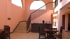 A hotel lobby with a staircase, a reception desk, and a dining area with chairs and a table. - Coco Beach Hotel (Sardinal)