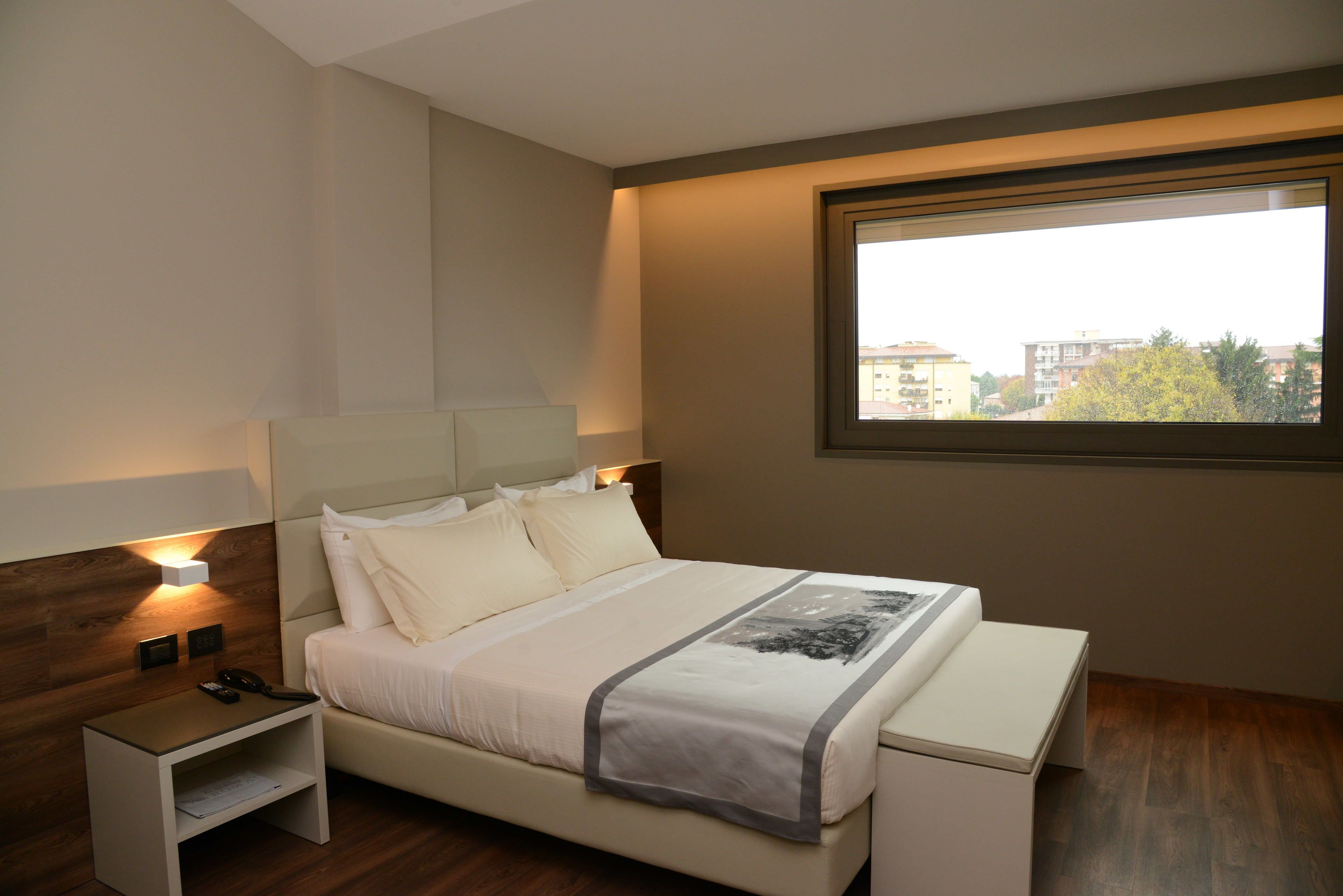 A modern bedroom with a bed, bedside tables, a nightstand, and a window with a city view.