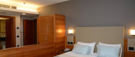 Habitación de hotel con una cama grande, armario de madera, lámparas de noche y mesita de noche.