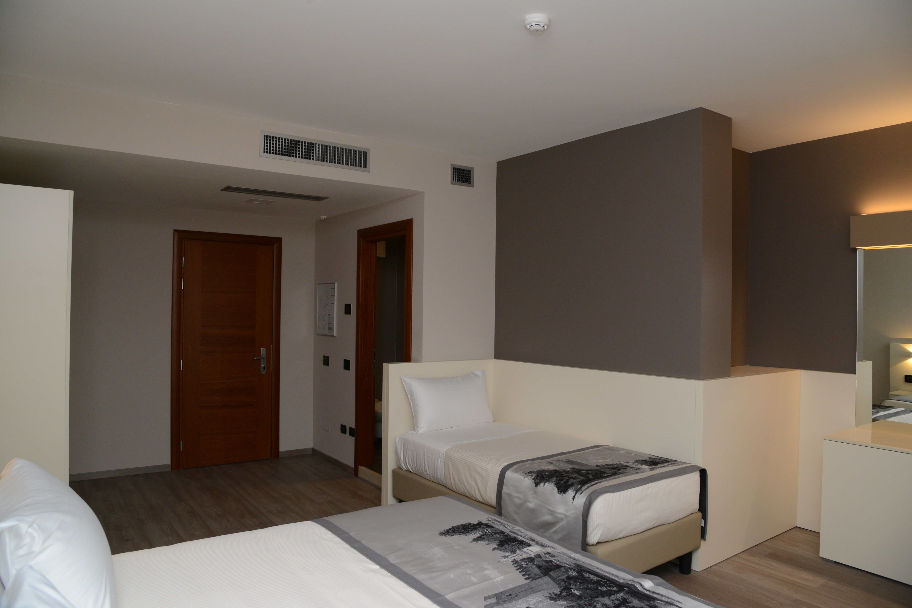 Habitación de hotel con dos camas, una puerta de madera, una mesita de noche blanca y un espejo grande.