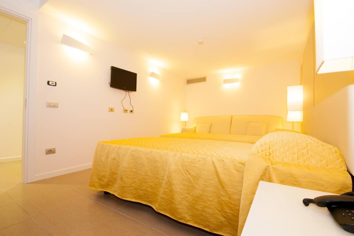 Een hotelkamer met een bed, bedlampjes, een telefoon en een aan de muur bevestigde televisie.