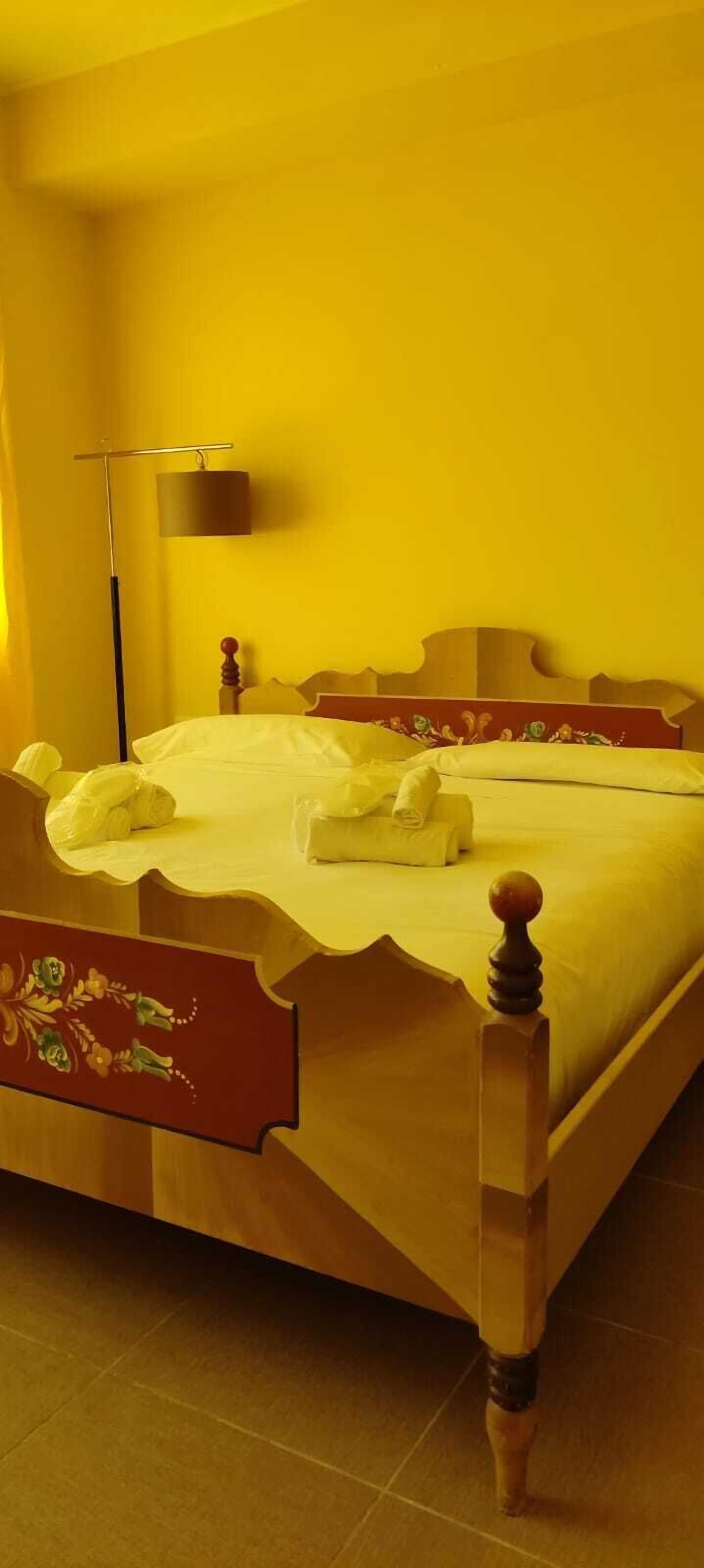 Un lit avec un cadre en bois et un motif floral, une lampe de chevet et un lit bien fait avec des serviettes.