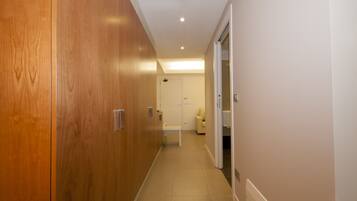 A hallway with wooden doors, a white bench, and a door leading to a room with a bed and a nightstand.