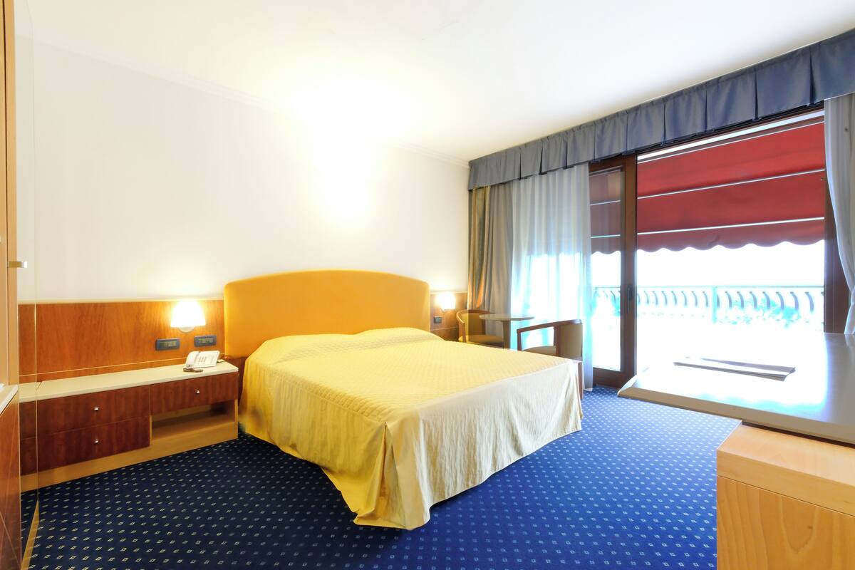 Een hotelkamer met een bed, nachtkastje, lamp en een raam met gordijnen.