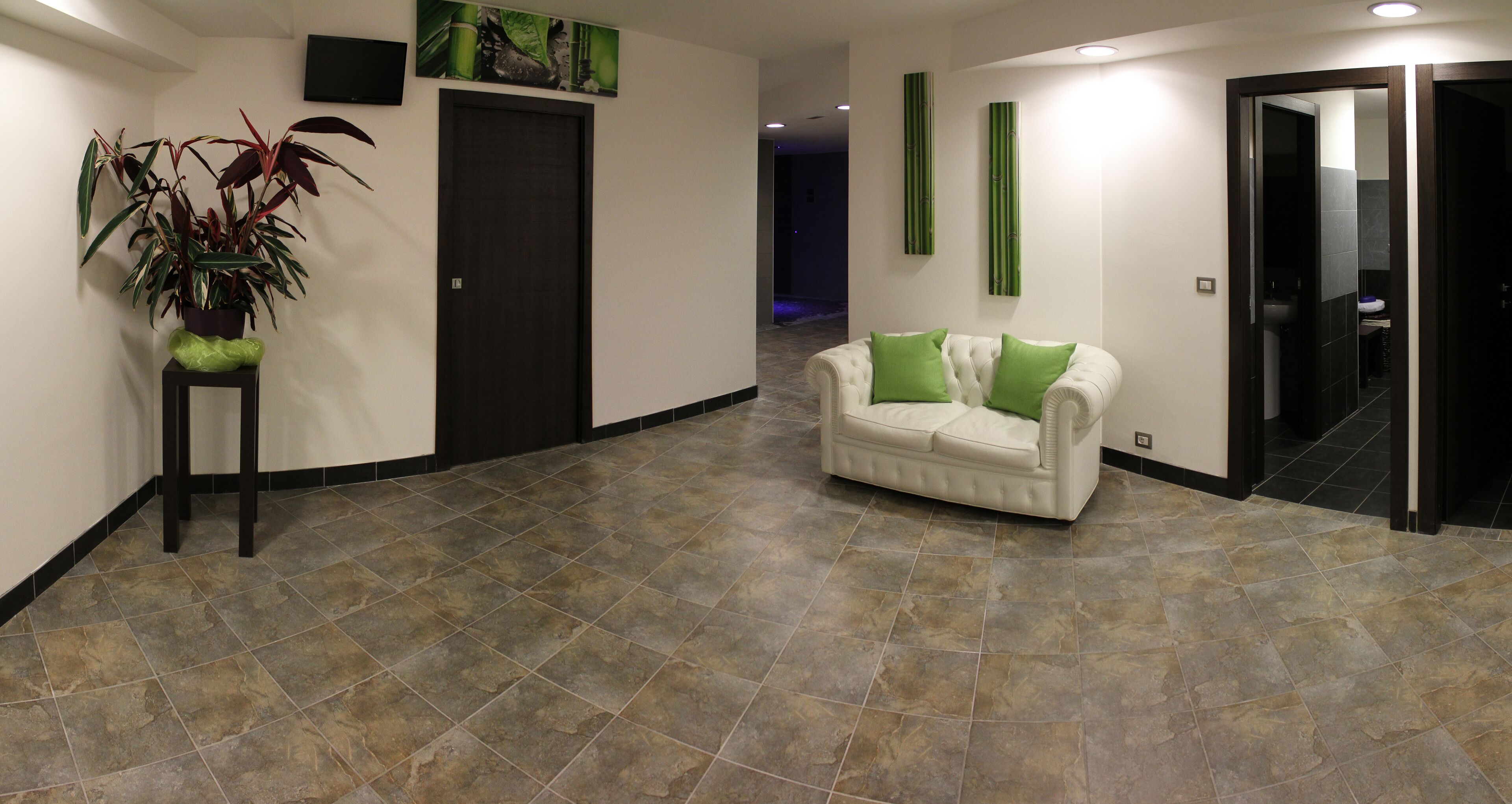 A modern lobby with a white sofa, green cushions, a potted plant, and a tiled floor.