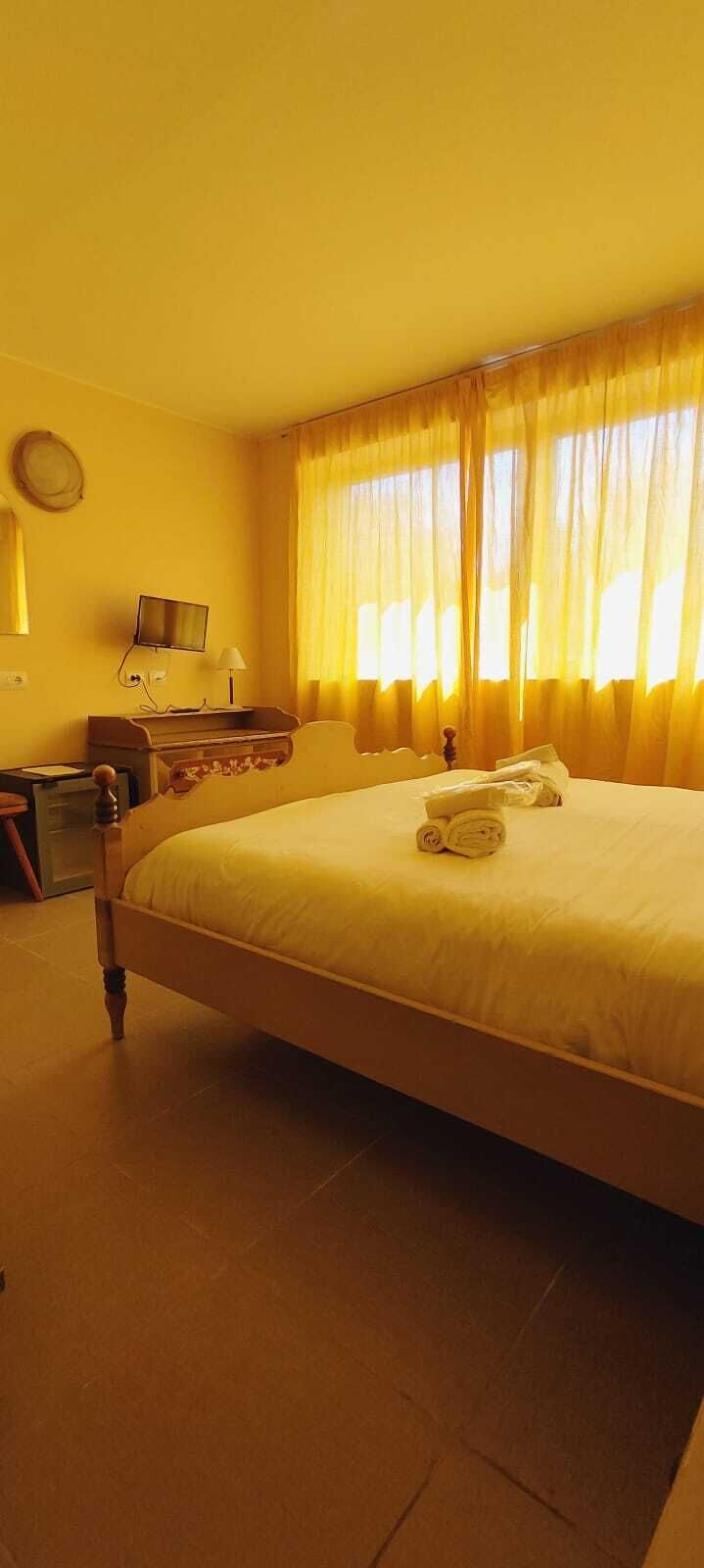 A hotel room with a large bed, a desk with a chair, a television, and a window with curtains.