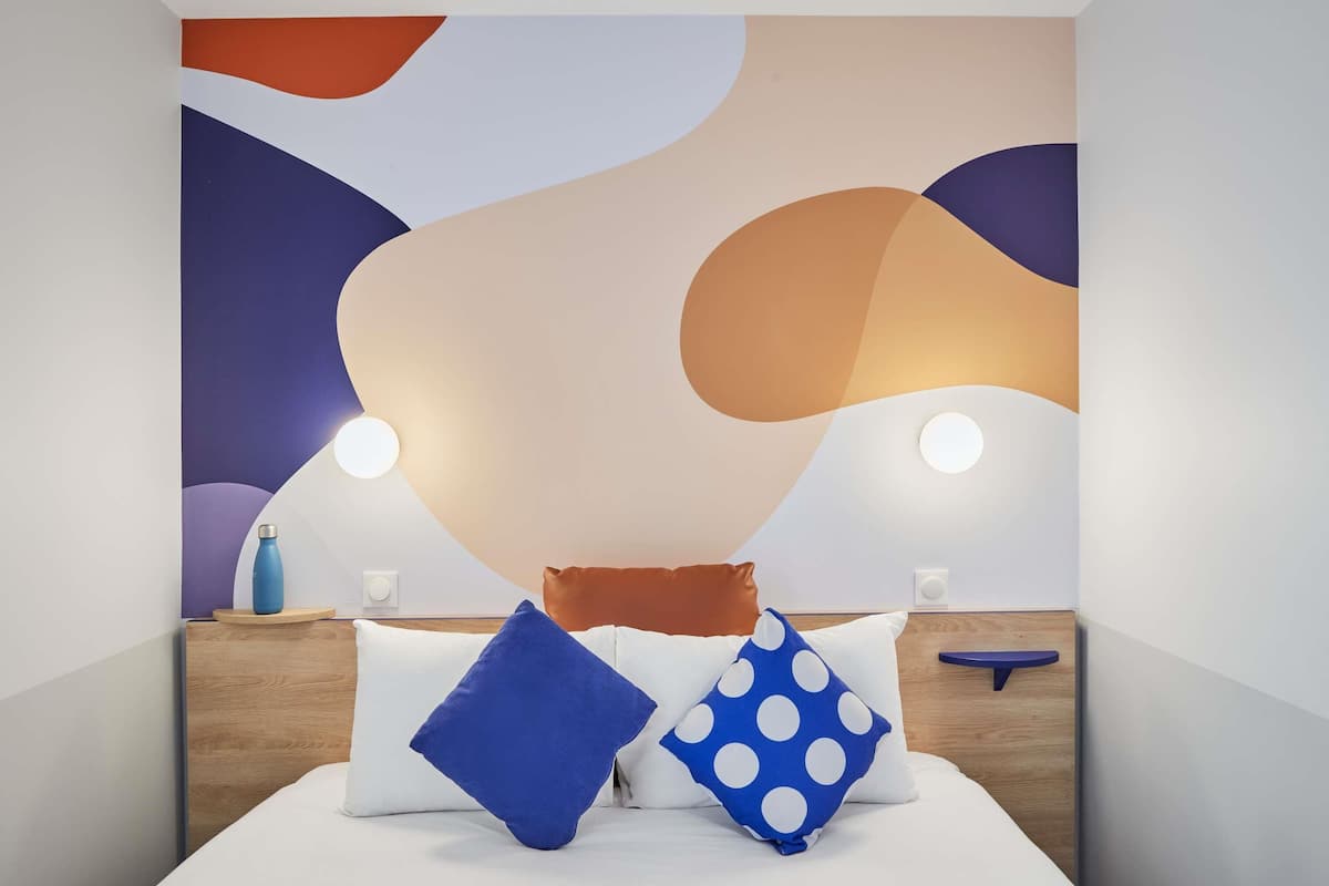A modern bedroom with a bed, pillows, bedside tables, and wall art.