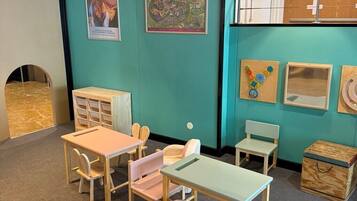 A children's playroom with teal walls, wooden furniture, and educational posters.