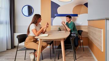 Una sala de reuniones moderna con una mesa redonda, dos sillas, una lámpara colgante y una pared con arte abstracto.