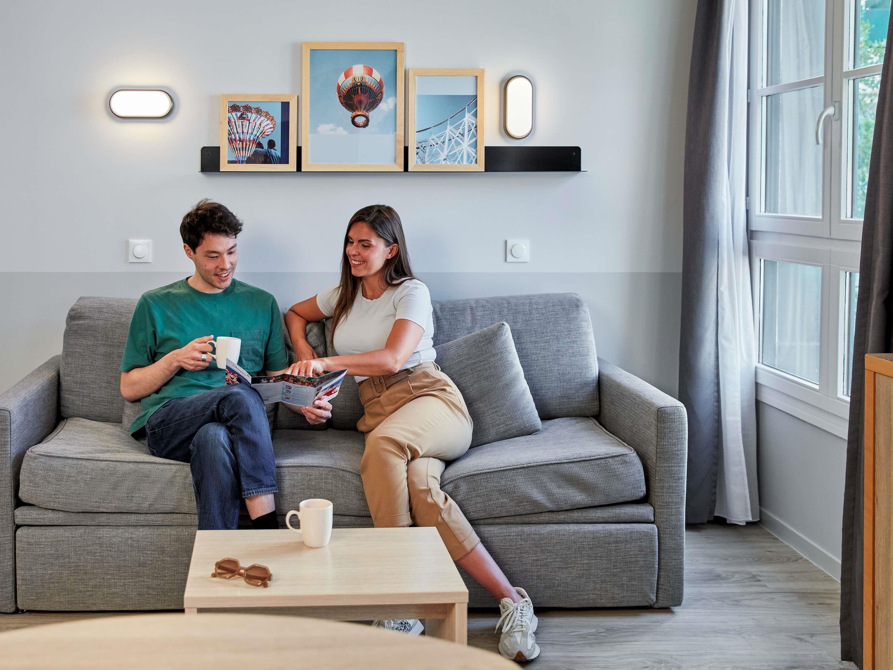 Ein modernes Wohnzimmer mit einem grauen Sofa, einem Couchtisch und einem Fenster mit Vorhängen.