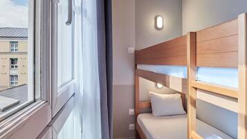 Una habitación de hotel con literas, una ventana con cortinas y una lámpara fijada a la pared.