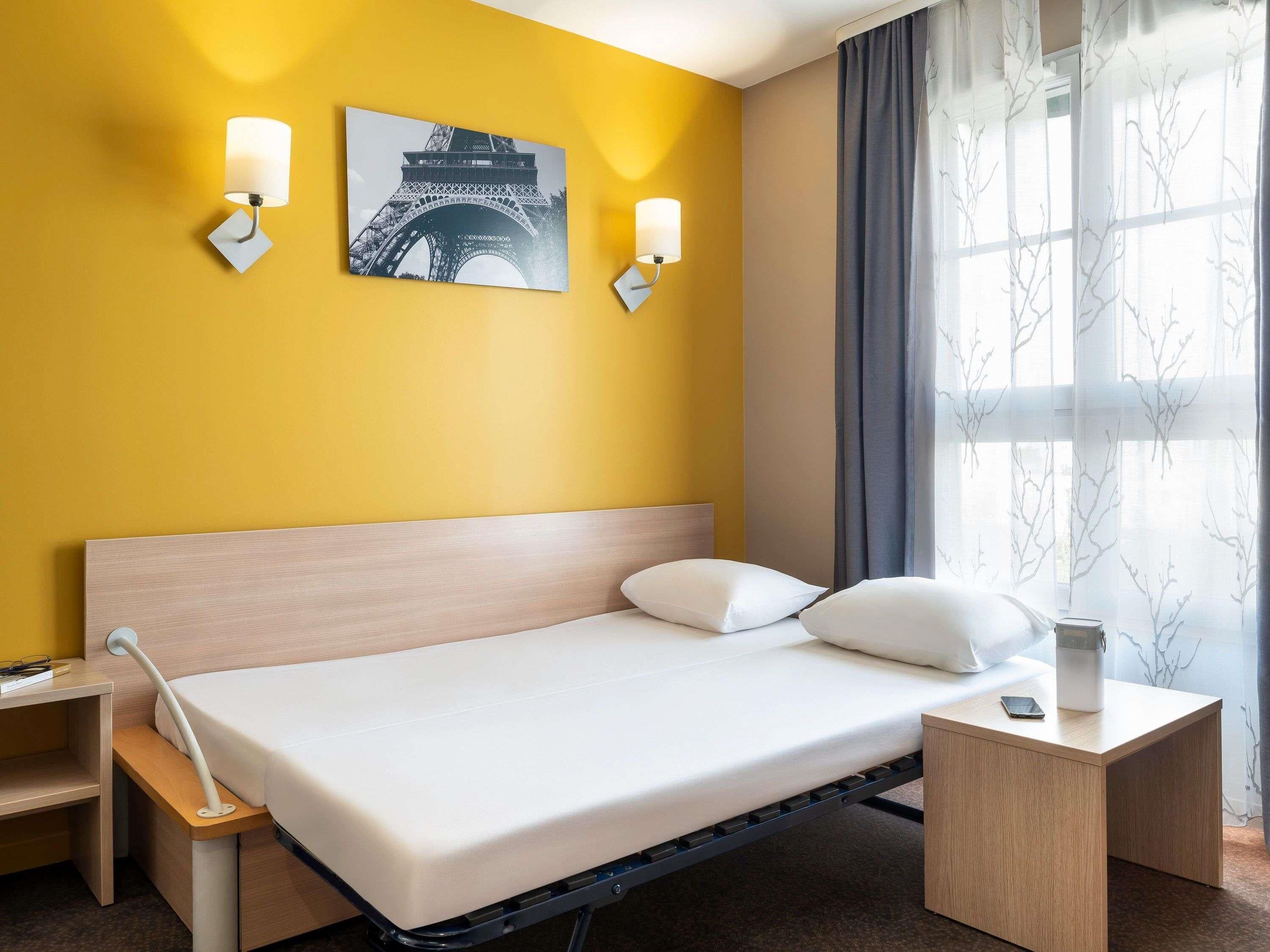 Une chambre d’hôtel avec un lit, des tables de chevet, une lampe et une image de la Tour Eiffel accrochée au mur.