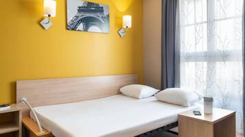 Une chambre d’hôtel avec un lit, des tables de chevet, une lampe et une image de la Tour Eiffel accrochée au mur.