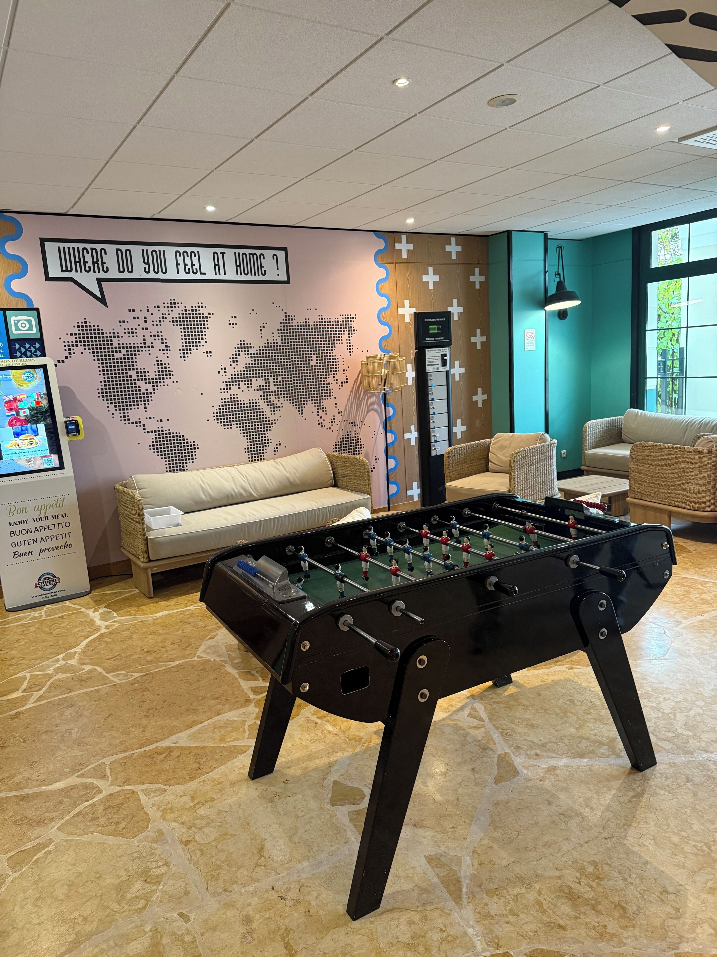 A foosball table in a room with a world map mural, a sofa, and a coffee machine.