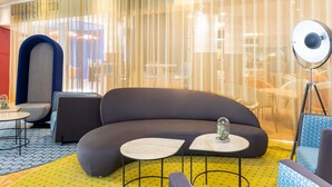 A modern lounge area with a curved sofa, small round tables, and a large floor lamp. - Aparthotel Adagio Val d'Europe près de Disneyland Paris (Serris)