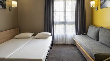 Une chambre d’hôtel avec un lit, un canapé, une fenêtre avec des rideaux et des lampes fixées au mur.