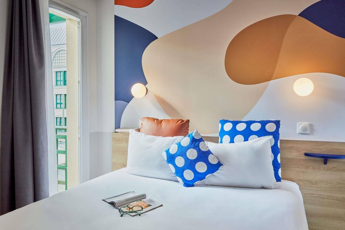 A hotel room with a bed, pillows, a magazine, and glasses.