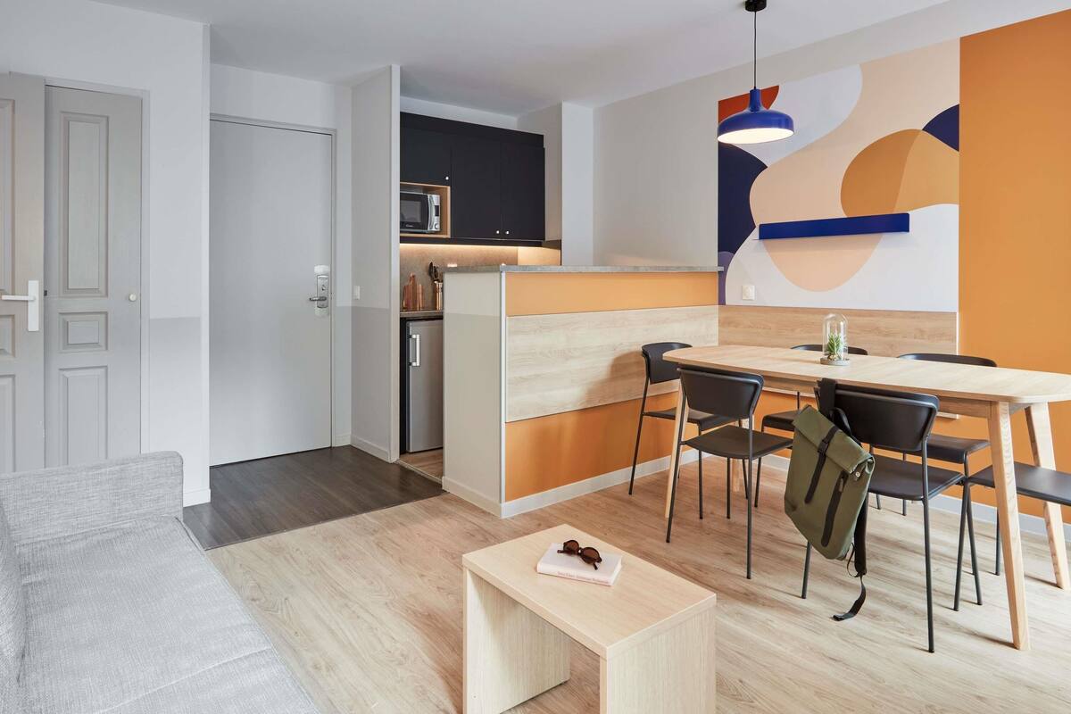A modern apartment with a dining area, kitchen, and a living room with a sofa and a small table.