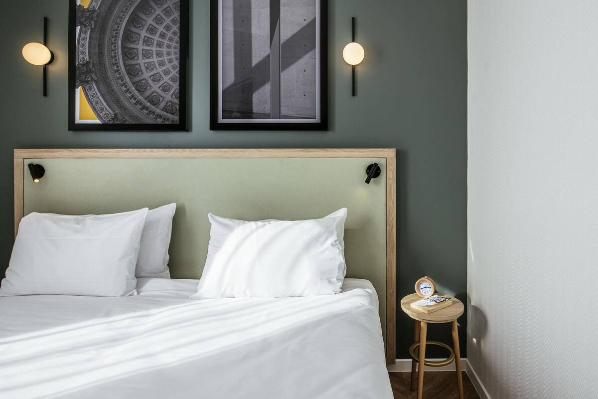 Una cama bien hecha con ropa blanca, cabecera de madera y dos lámparas fijadas a la pared.