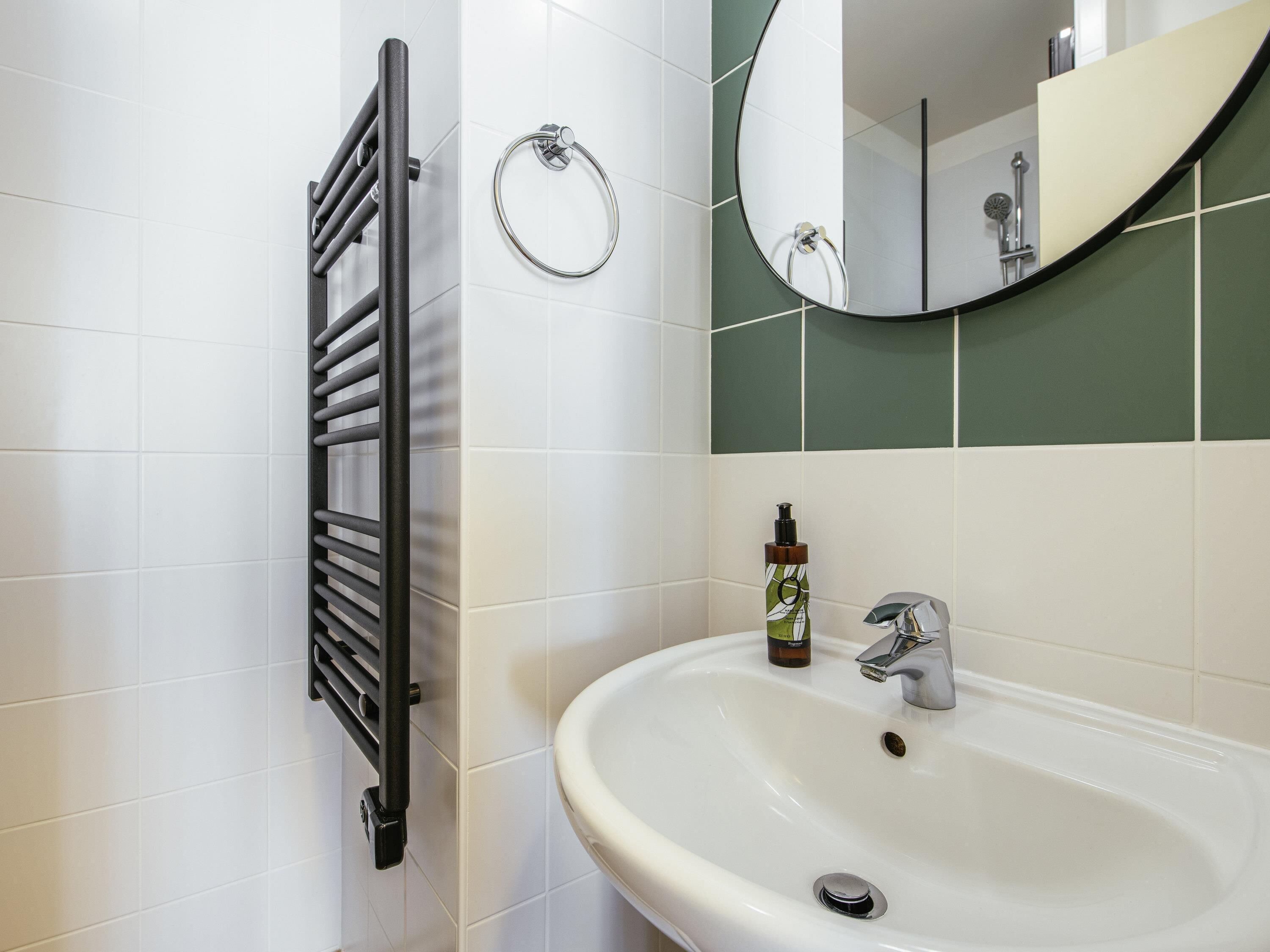 Une salle de bain avec un lavabo blanc, un miroir, un porte-serviette et un étendoir à serviettes.