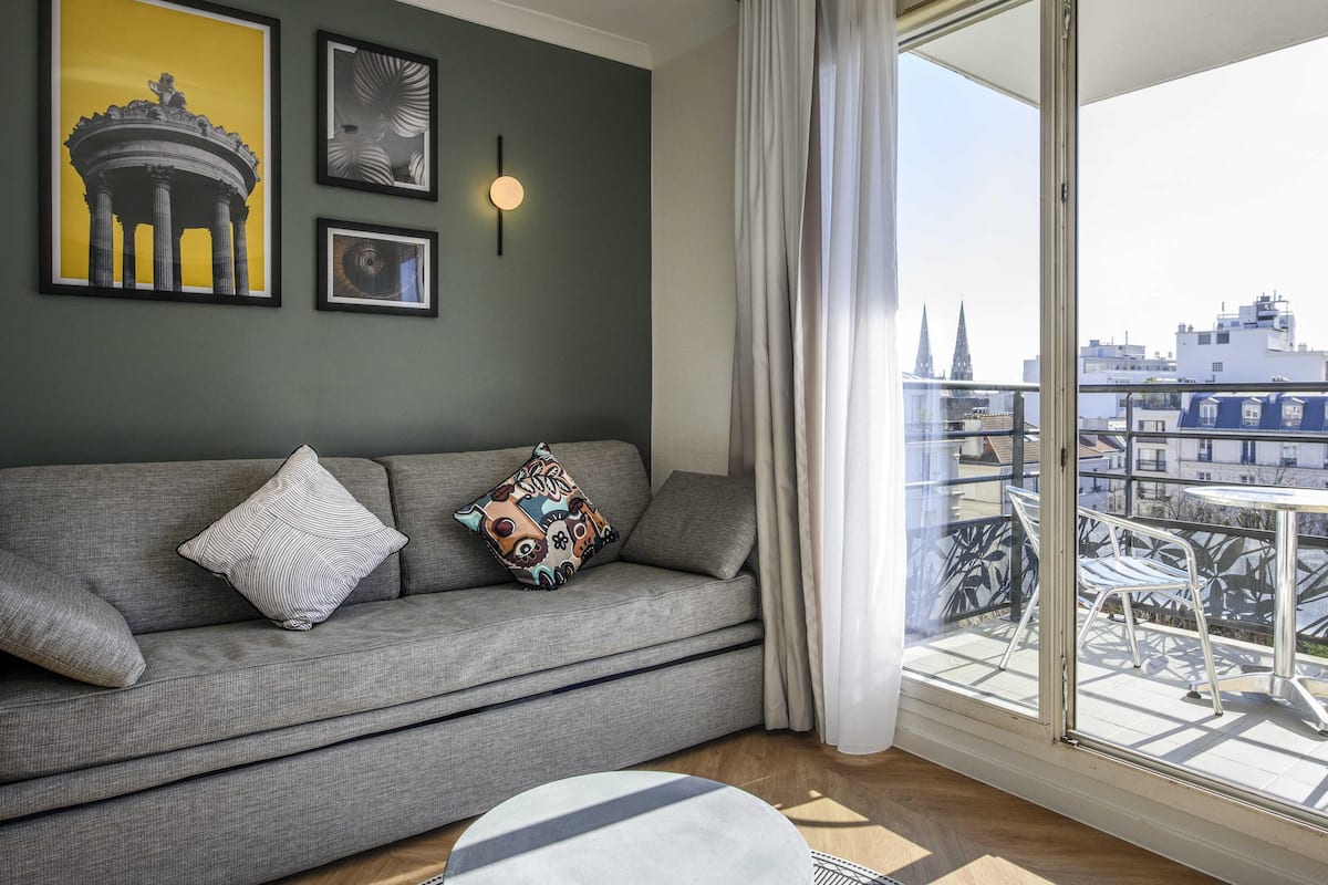 Una sala de estar moderna con un sofá gris, cojines estampados y cuadros en la pared.